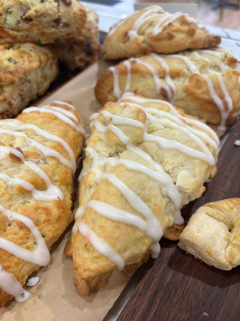 Golden-brown baked scones with white drizzle, arranged on a wooden board with parchment paper.
